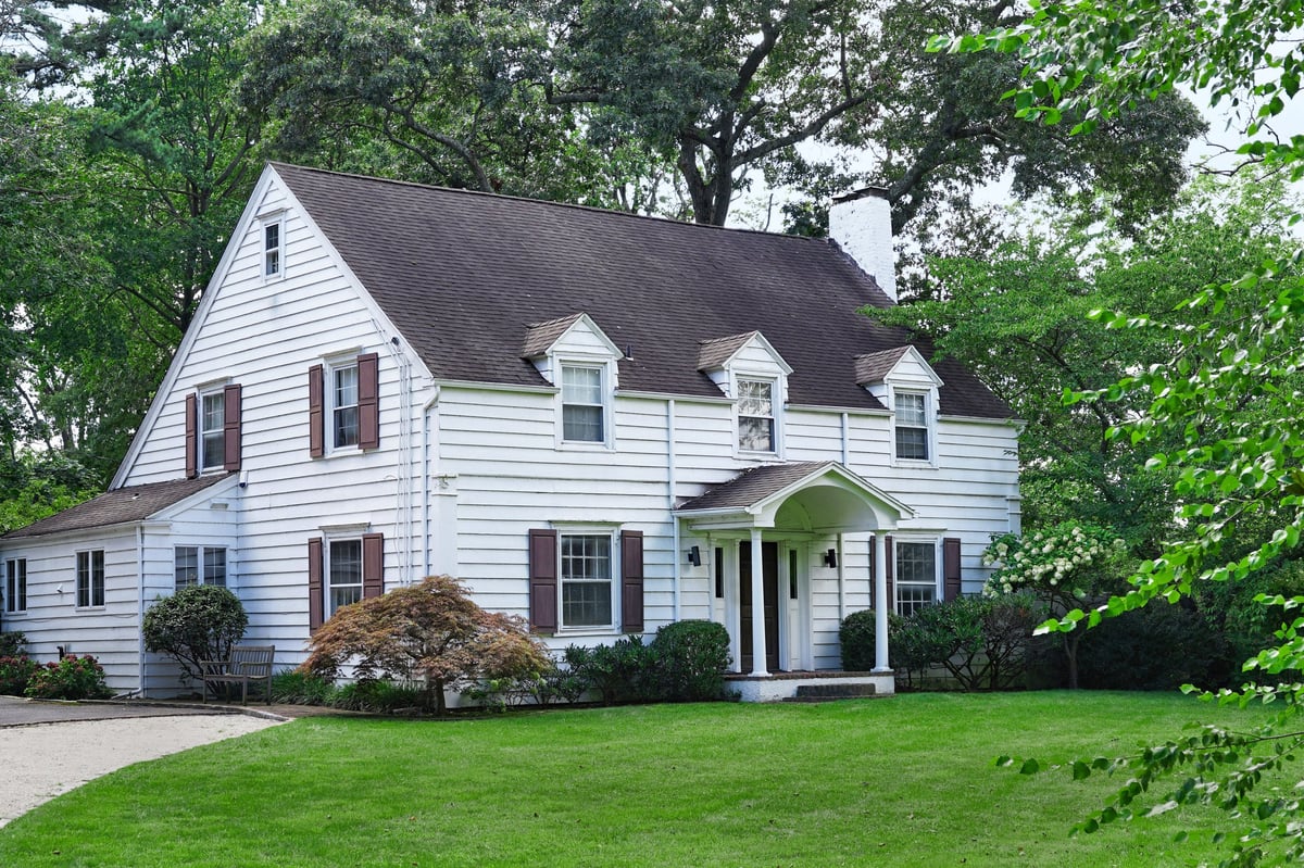 Two story clapboard house surrounded by mature trees, full front view