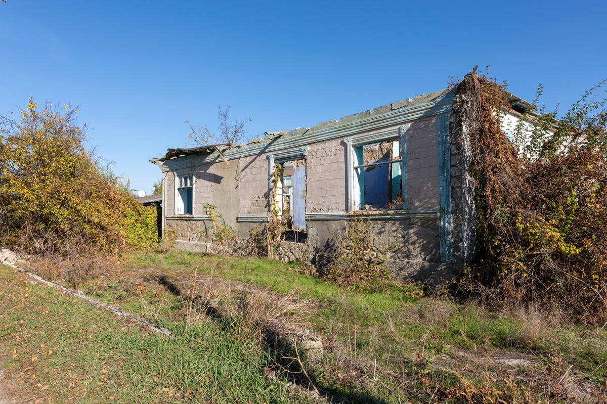 Old deserted house with peeling paint and overgrown vegetation, needs work